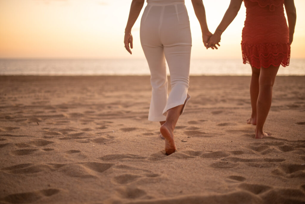 Ein weibliches Paar geht Hand in Hand auf das Meer zu - Link zur Paartherapie